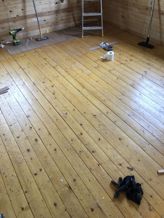 Obehandlat furugolv i behov av slipning, med verktyg och byggmaterial utspridda i ett rum under renovering.