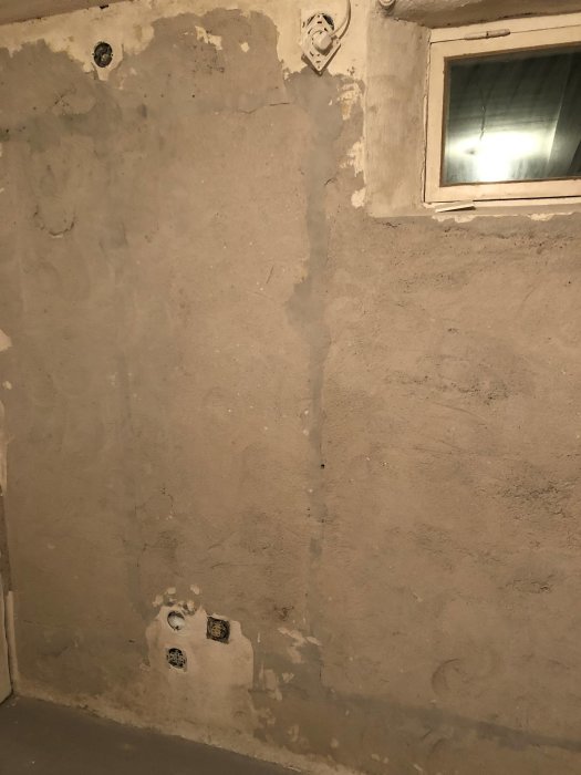 Källarrum med delvis slipade väggar, synliga eluttag och ett litet fönster.