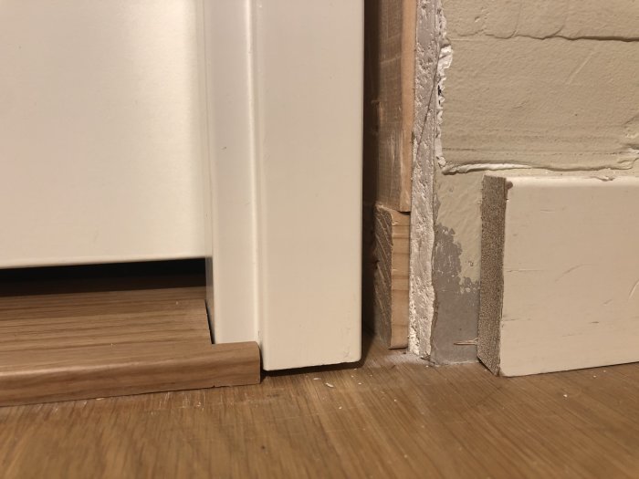 Ojämnt mellanrum under en vit dörrkarm och golv, med synlig höjdskillnad och tröskel.