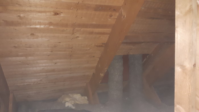Inre snedtak av råspont i äldre hus med synliga takbjälkar och isolering mellan reglarna.