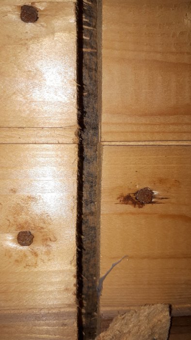 Närbild på råspont och svart papp i en huskonstruktion från 70-talet, synlig genom rivna tretexplattor.