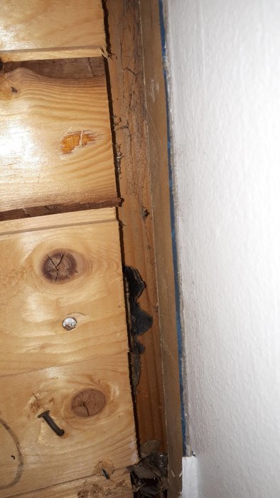 Råspont och isolering i hörn av ett gammalt hus med synliga naglar och svart papp.