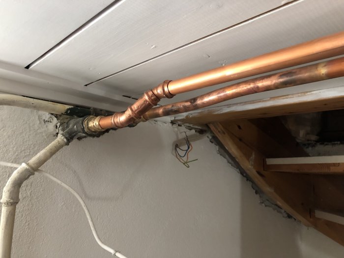 Renoverad vägg med plåtreglar, byggplywood och nymålade rör som böjts för att ansluta gamla och nya rörledningar.