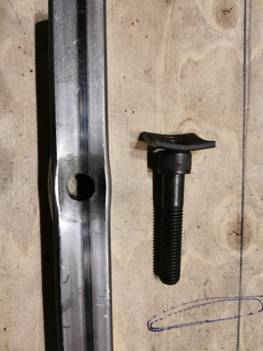 Deformerat metallrör och en skruv bredvid skisser på en träytvägg, test av styrka och passform.