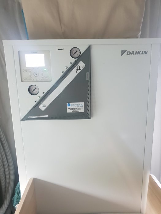 Bergvärmepump från Daikin med display och två tryckmätare som visar 0, monterad inomhus.