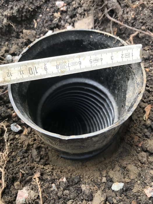 Måttband som mäter diameter på änden av ett svart 110 mm dräneringsrör i marken.
