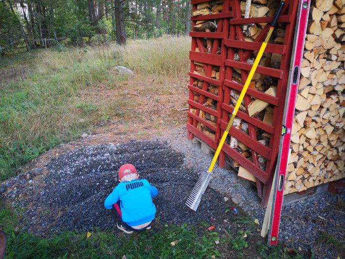 Aluminiumkratta lutad mot vedställ med barn som arbetar i grus, omgiven av skog och gräs.