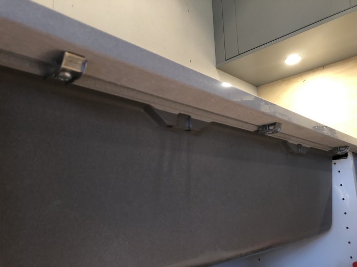 Klammor som fäster köksluckans front underifrån mot en bänkskiva.
