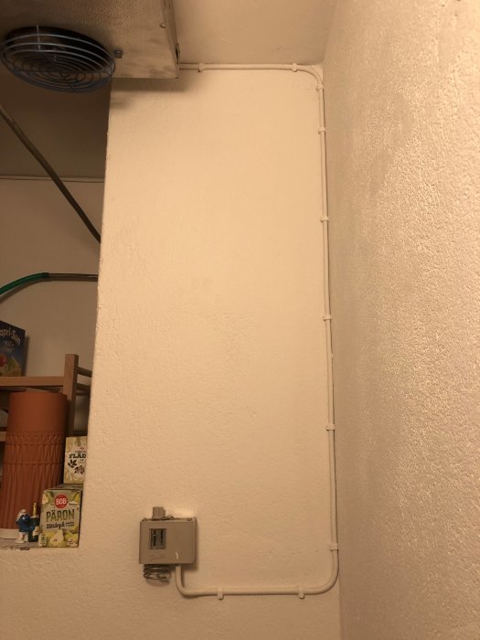 Kylrumsutrustning med slangar och termostat på en vägg ovanför lagringshyllor.
