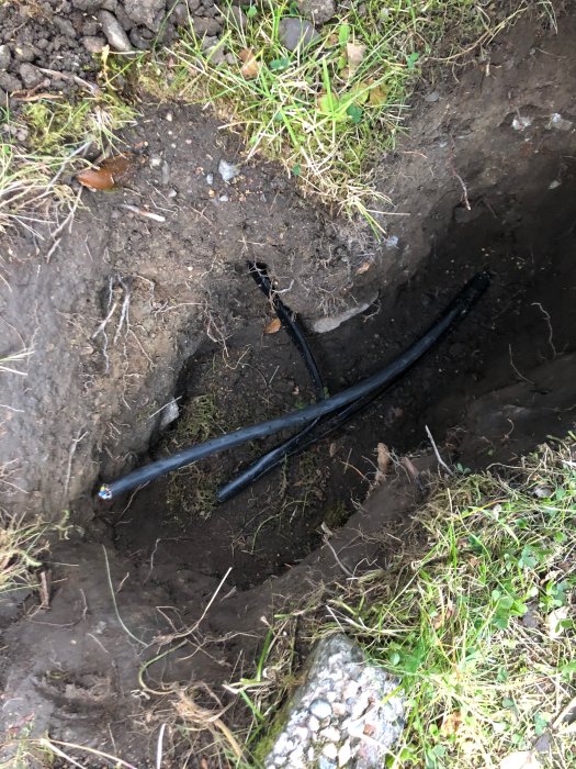 Ett grävt hål i jorden med elektriska kablar lagda bredvid varandra, visar pågående arbete med underjordisk kabeldragning.