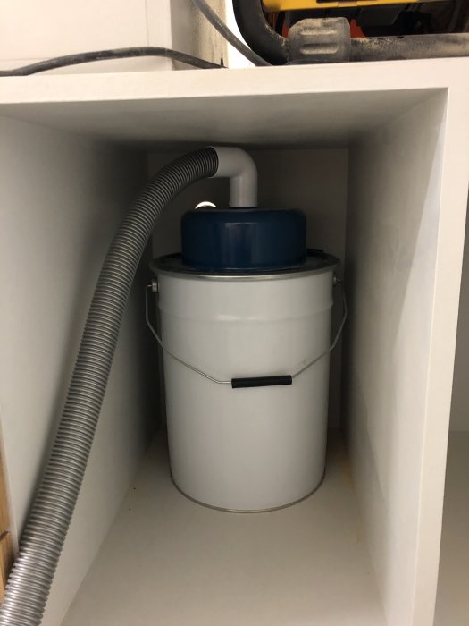 DIY-sågskalas cyklonstystem med ansluten dammsugarslang och hink inuti ett skåp.