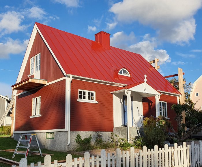 Nästan färdigt rött hus med nytt rött tak och vit snickarglädje, stegar vid sidan.