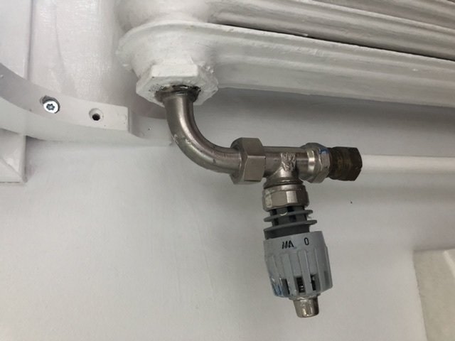 Termostat på ett vitmålat element med en metallanslutningsrör och inställningsratt indikerande noll.