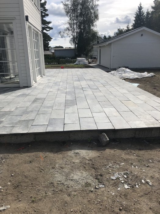 Nyinstallerade ljusgrå plattor på en uteplats med tät fogning, angränsande till en vit husvägg och garage.