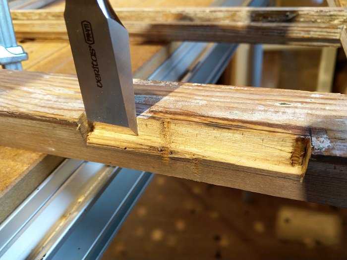 Stämjärn som används för att jämna ut ett urtag i en gammal fönsterbåge med synliga skador och sprickor.