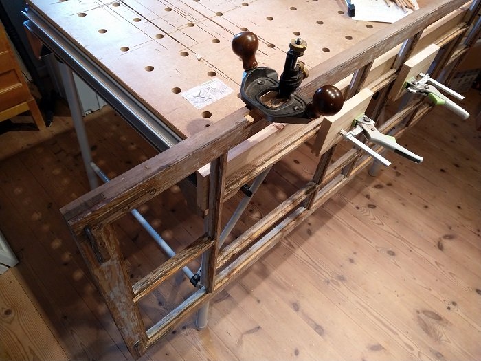 Gammal fönsterbåge på arbetsbänk med en handhyvel och klämmor, redo för reparation.