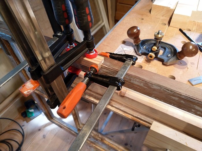 Reparation av spräckt trä på ett gammalt fönster med klämmor, lim och verktyg på en arbetsbänk.