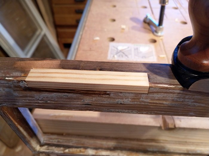 Nysågad träbit infälld i gammal fönsterbåge för reparation av spräckt trä.