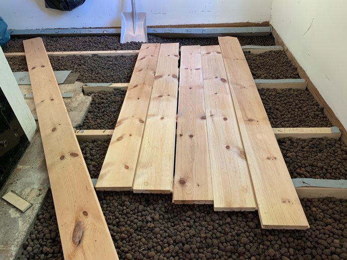 Uppriven trägolv med synliga träreglar och Leca-kulor som isolering i krypgrund.