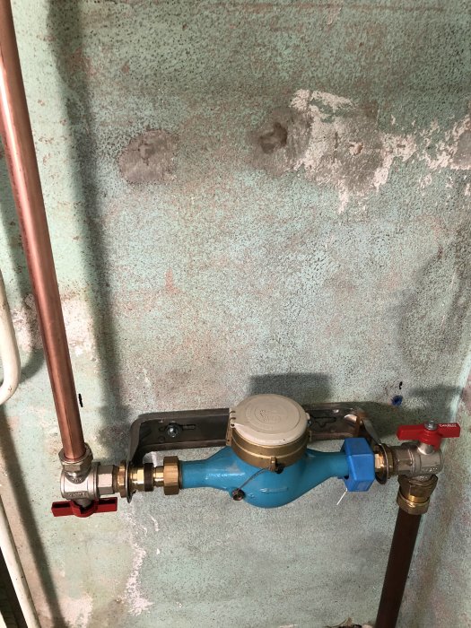 Vattenmätare med anslutna kopparledningar monterade på en vägg med avskalad färg.