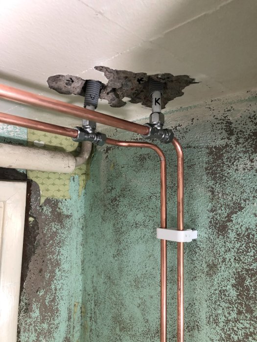 Nya kopparledningar för tappvatten installerade i ett hörn med märkning och fästen mot en fuktig vägg.