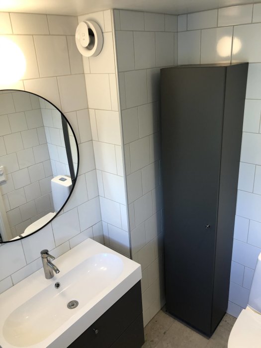 Renoverat badrum med vit tvättställ, spegel, grå duschvägg och IFÖ lampa.