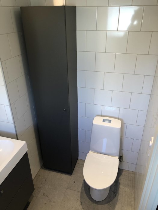 Modernt badrum med toalett, dörr till duschvägg och handfat, nyinstallerade vitvaror och kakel.