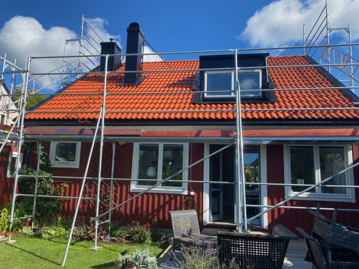 Rött hus med nytt tak och ställning runt fasaden, synliga takpannor och takfönster.