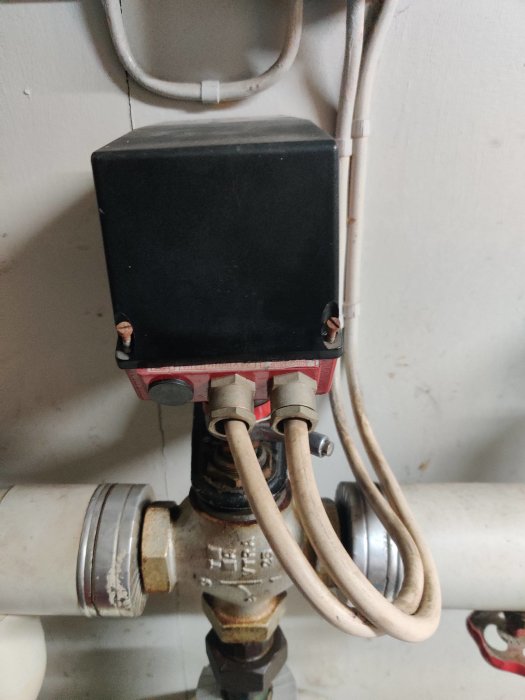 Shuntventil med svart manöverenhet och anslutna kablar installerad på vattenrör, diskussion om byte av modell.