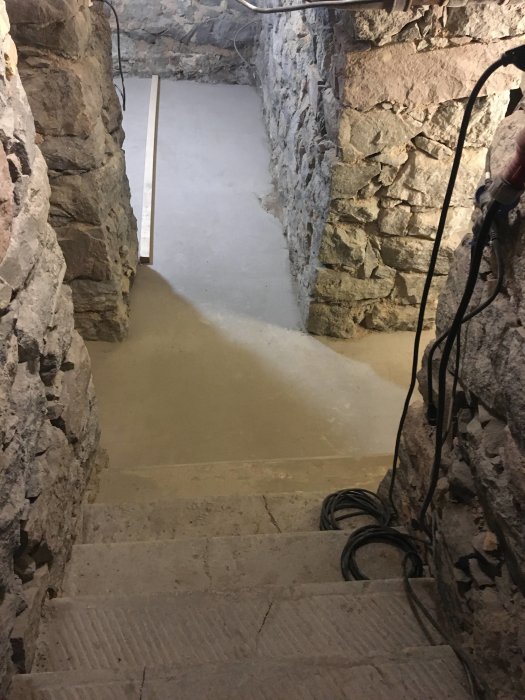 Nyligen gjutet betongtrappsteg och golv i ett stenrum som blir ett badrum.
