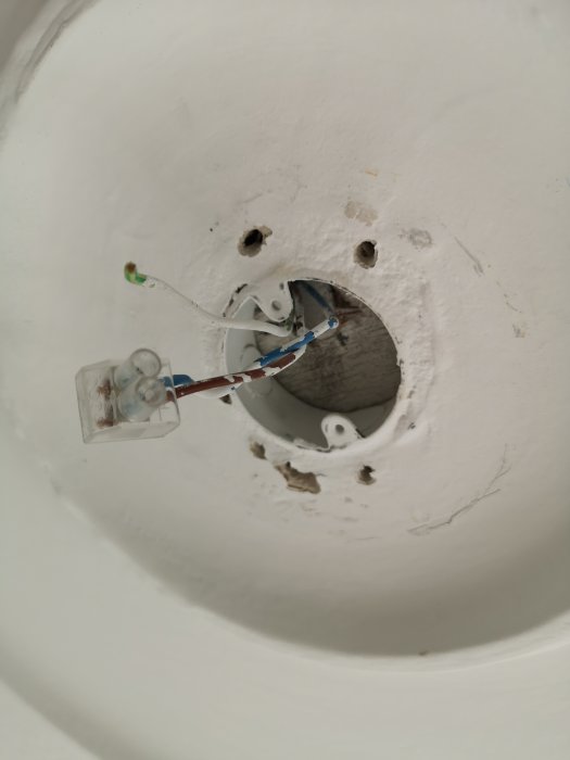 Vy uppåt av ett öppet lamputtag i taket med exponerade ledningar och en ringformad fästdel med två gängade hål.