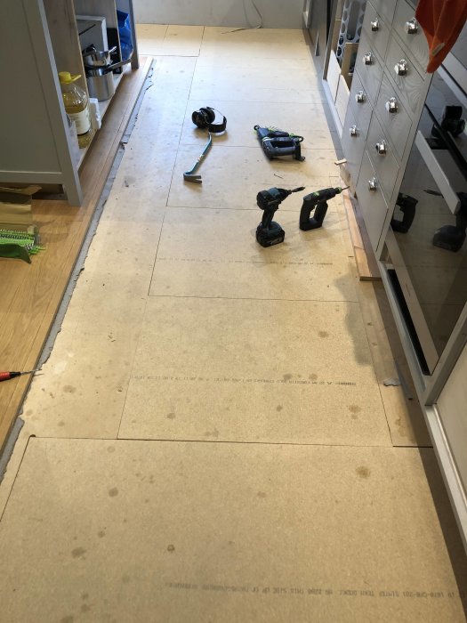 Ej färdigt köksgolv med plywood och utspridda verktyg under renovering.