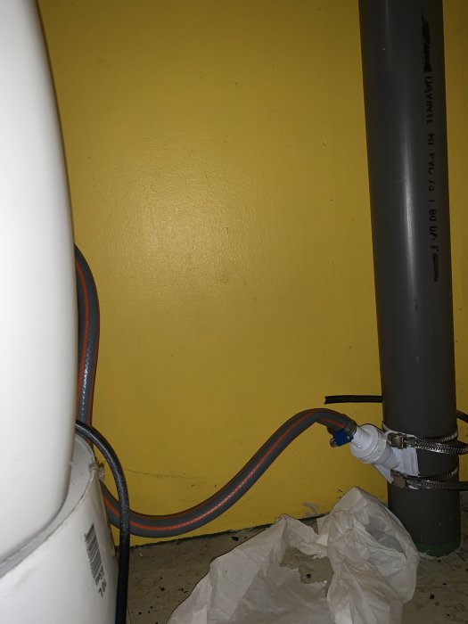 Rörinstallation mot gul vägg som möjligt vattenlås med kablar och rör på betonggolv.