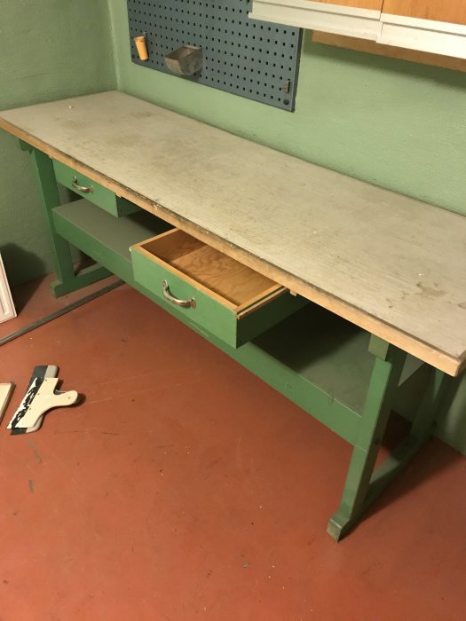 Arbetsbänk med utdragen låda i ett pannrum, verktygstavla med krokar på väggen.