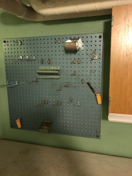 Verktygstavla med krokar på grön vägg i pannrum, några verktyg och skåp synliga.