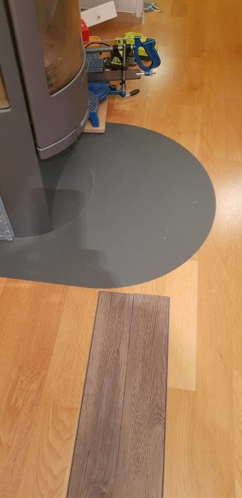 Ny lagt laminatgolv intill befintlig parkett vid en braskamin, med tydlig nivåskillnad.