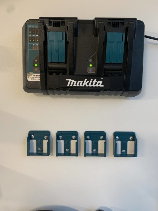 En Makita dubbelladdare på väggen med två batterier i och fyra blåa batterihållare monterade nedanför.