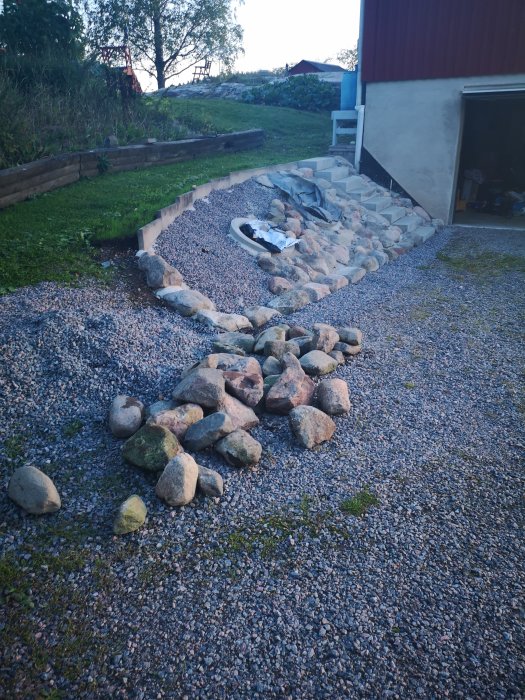 Stenlänt med grus, stenar i olika storlekar och avslutade arbeten vid husvägg och gräsmark.