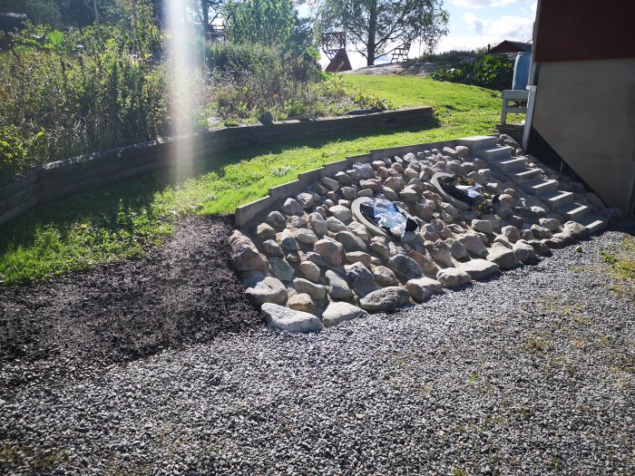 Upprustad slänt med stenläggning, grus och trappsteg i soligt väder.