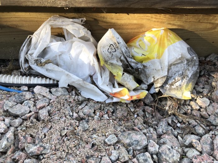 Eldosor till poolbelysning inkapslade i sönderrivna plastpåsar på grusmark under trädäck.