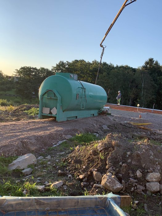 Betongarbete pågår med en stor grön betongbil och en arbetare som övervakar gjutningen.