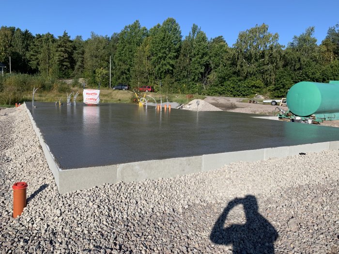 Nyutgjuten betongplatta med vattenspridare och betongpumpbil i bakgrunden.