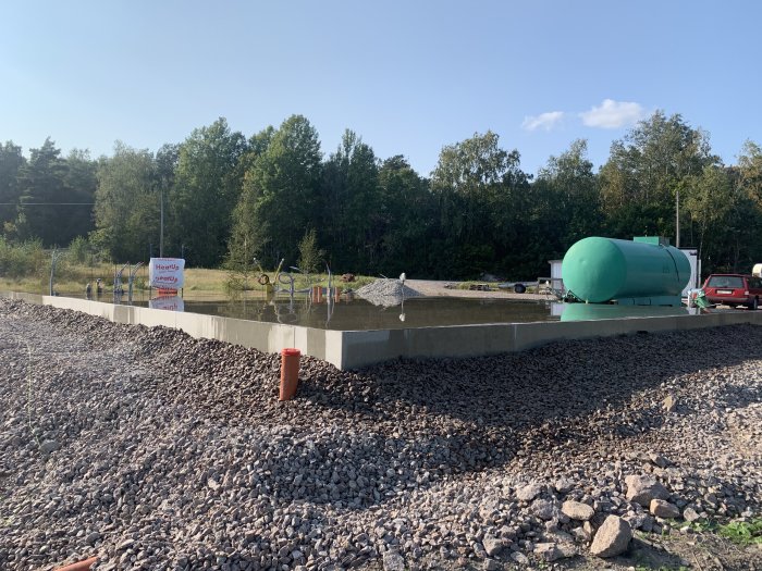 Nybetongad grund med skottkärror och en grön vattencistern i bakgrunden på en byggarbetsplats.