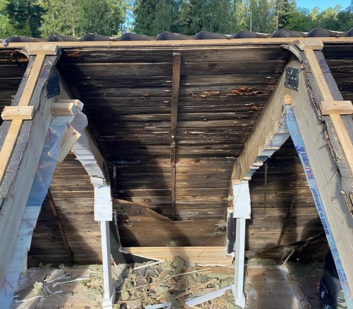 Rivet innertak med synliga takstolar och fuktskador på en träkonstruktion, utan vind.
