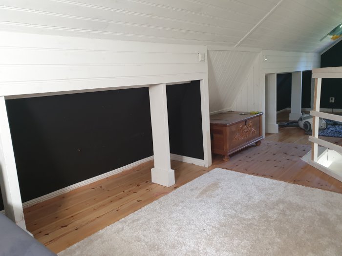 Vardagsrum med vitmålade snedtak, trägolv och oinredda vägginfällningar innan rivning.