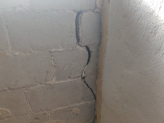 Vägg med porös puts och en stor spricka i hörnet där bruket är sandigt.