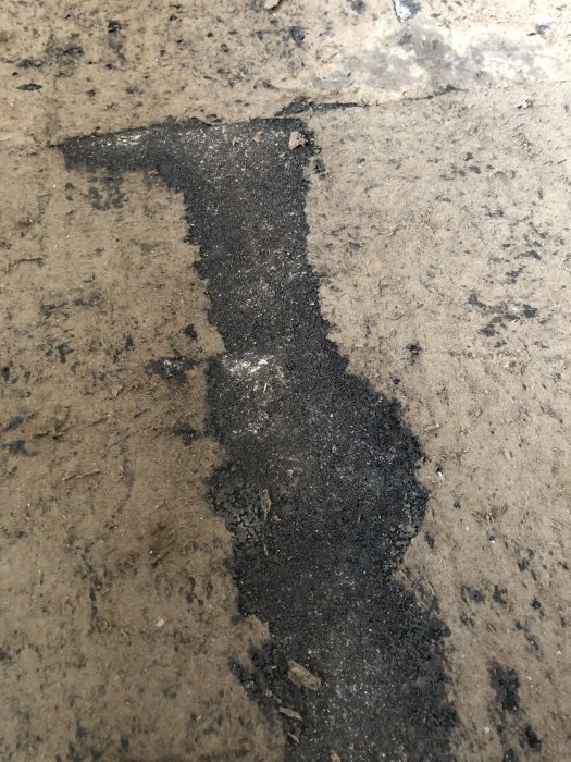 Betonggolv i källare med rester av svart lim efter borttagen plastmatta, möjligt asbesthaltigt material.