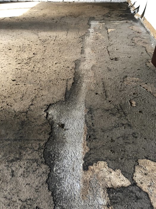 Betonggolv i källare med rester av gammalt svartlim och pappersrester efter borttagen plastmatta.