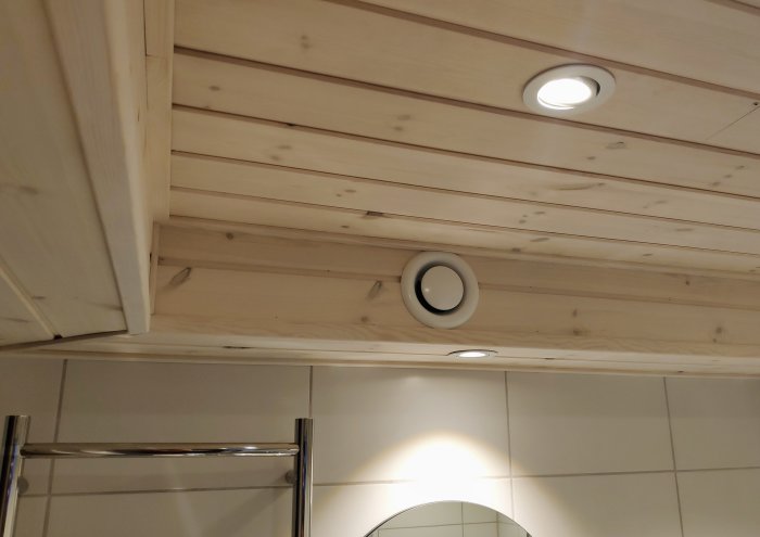 Trätak med infällda spotlights och en nyinstallerad takventil, omgivet av en komplex taklistning.