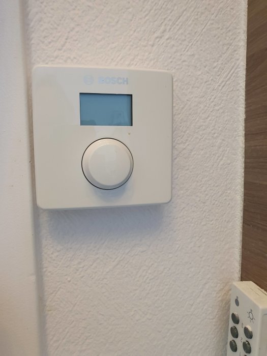 Bosch CR10/EMS 2 termostat med tom display monterad på en vit vägg, intill en annan strömbrytare.